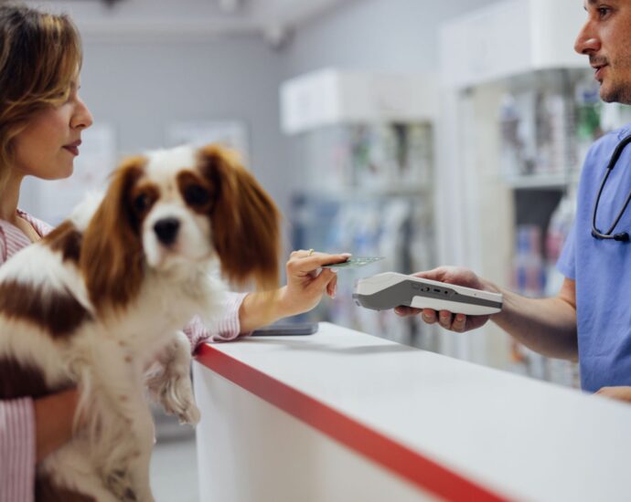 Pet owner paying for services at a veterinary clinic reception desk while holding a small dog